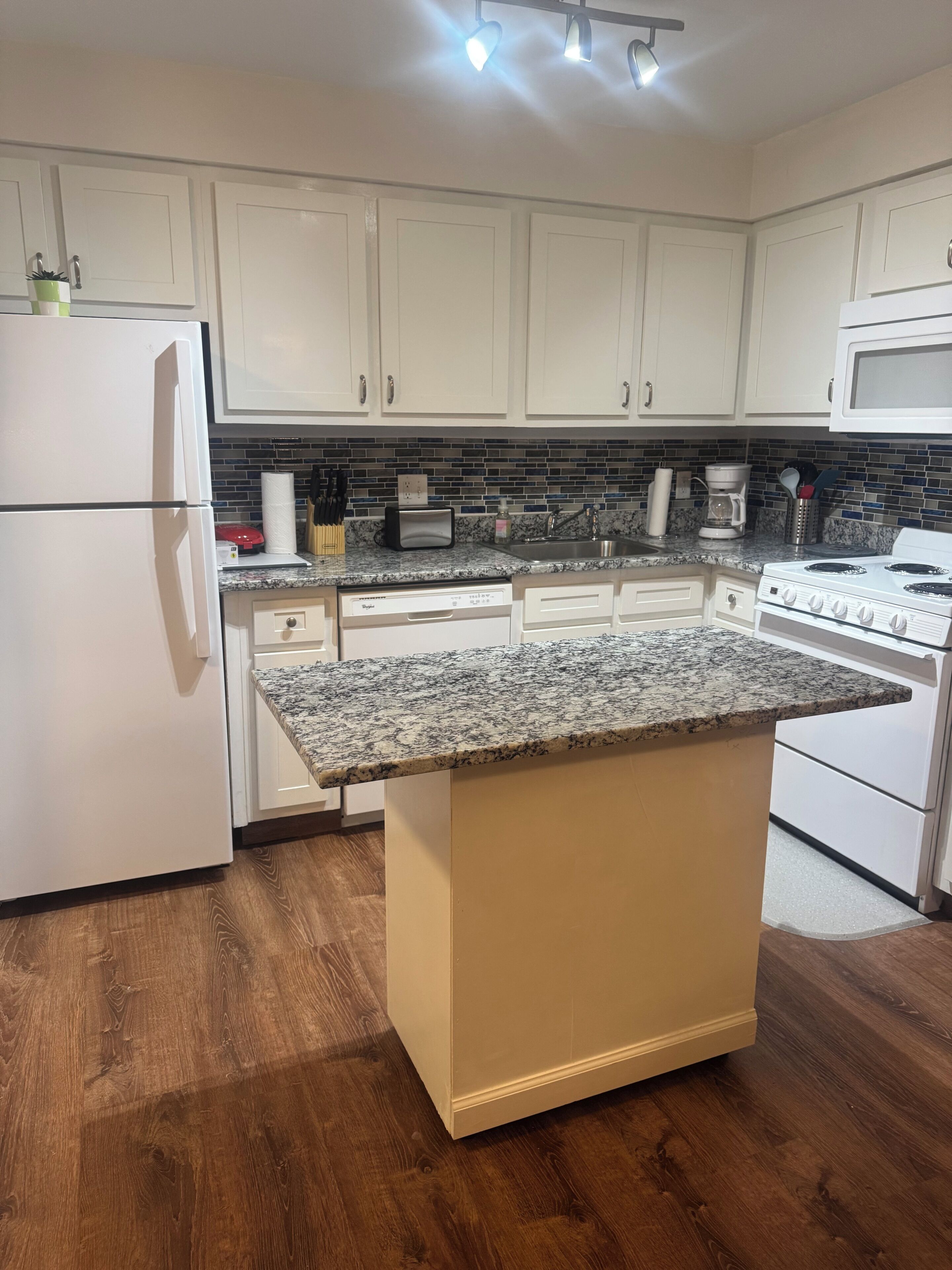 A kitchen with white cabinets, a granite countertop island, a built-in oven, and a microwave.
