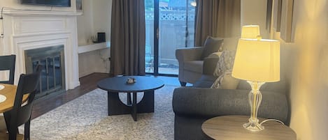 A living room with a fireplace, a television mounted above it, a sofa, a coffee table, and a lamp.