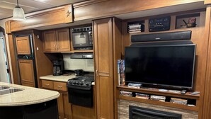 A compact RV kitchen with a stove, coffee maker, and a flat-screen TV mounted on the wall.