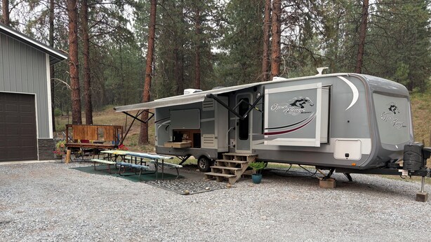 A recreational vehicle with a covered dining area, a small porch, and a storage compartment.