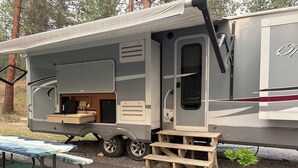 A recreational vehicle with an open kitchen area, a small dining table, and a set of wooden steps leading to the entrance.
