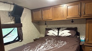 A bedroom with a bed, wooden cabinets, a television mounted on the wall, and a window with curtains.