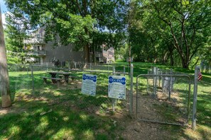 Un parc canin clôturé, équipé de tables de pique-nique et d’un panneau indiquant les règles et les coordonnées à contacter.