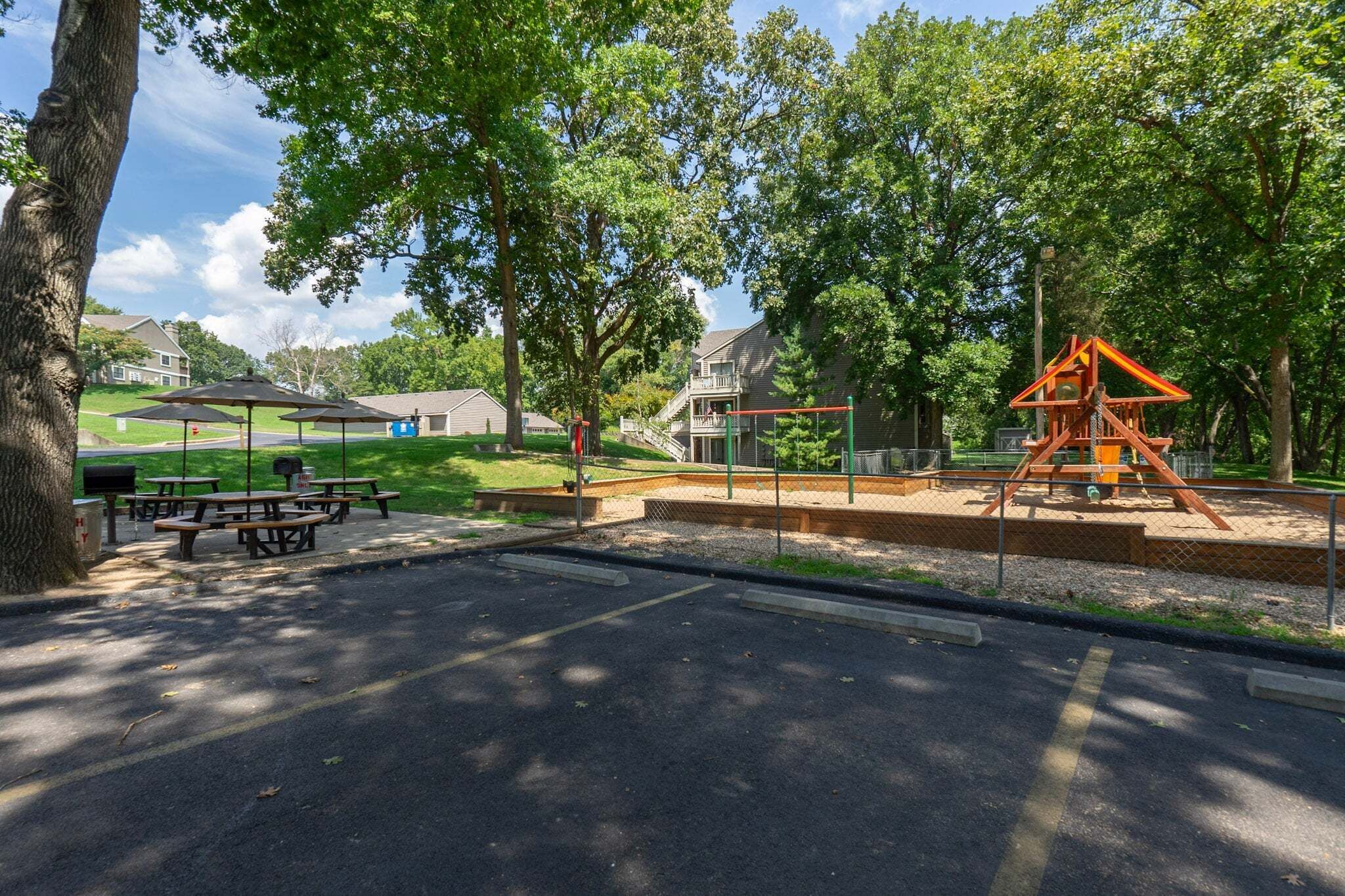 A park with picnic tables, a playground, and houses in the background.