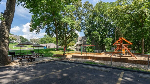 Un parque con mesas de picnic, un parque infantil y casas al fondo.
