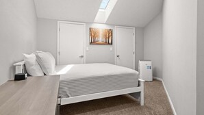 Un dormitorio con cama, escritorio, un cubo de basura y un tragaluz.