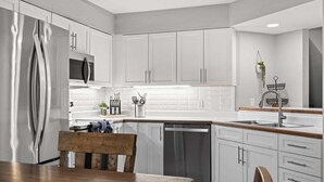 Una cocina moderna con armarios blancos, electrodomésticos de acero inoxidable y una mesa de comedor de madera.