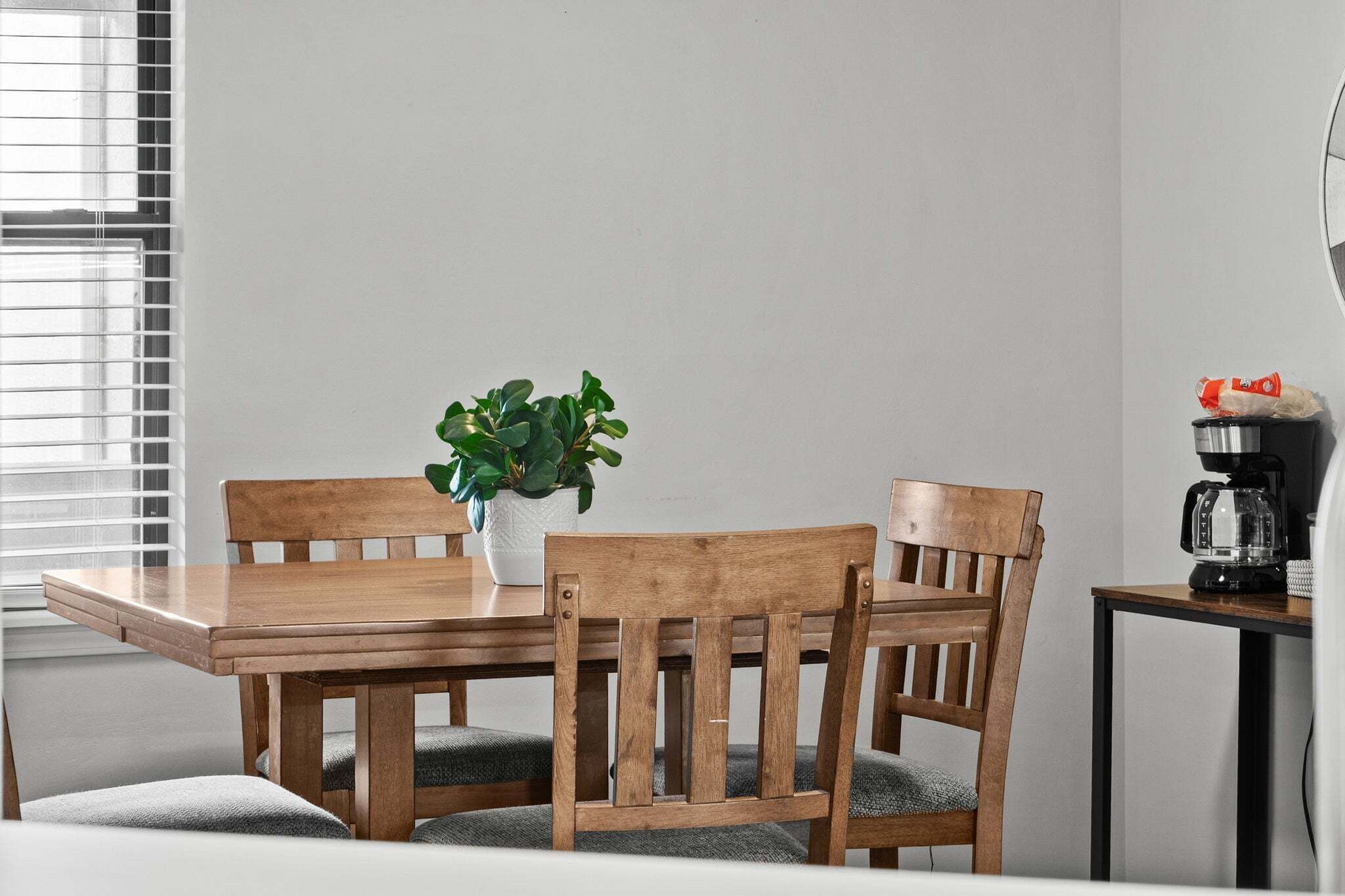 A dining table with two wooden chairs, a potted plant, and a coffee machine.