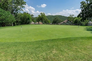 A golf course with a flag, trees, and buildings in the background. - Caddy Shack | Pointe Royale 3BR Condo w/ Pools + Golf Views (PR 61-8) (Branson)