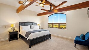 A bedroom with a large bed, two bedside tables, a ceiling fan, a large window with a view, and a blue chair. - Krisyn Vineyards by Avantstay Private Pool + Spa Templeton Wine Country (Templeton)
