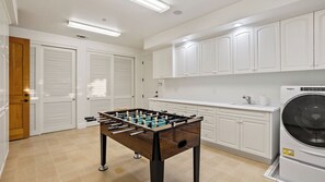 A clean, modern kitchen with white cabinets, a foosball table, and a Whirlpool washing machine. - Krisyn Vineyards by Avantstay Private Pool + Spa Templeton Wine Country (Templeton)