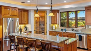 A modern kitchen with a central island, stainless steel appliances, wooden cabinets, and a large window offering a view of the outdoors. - Krisyn Vineyards by Avantstay Private Pool + Spa Templeton Wine Country (Templeton)