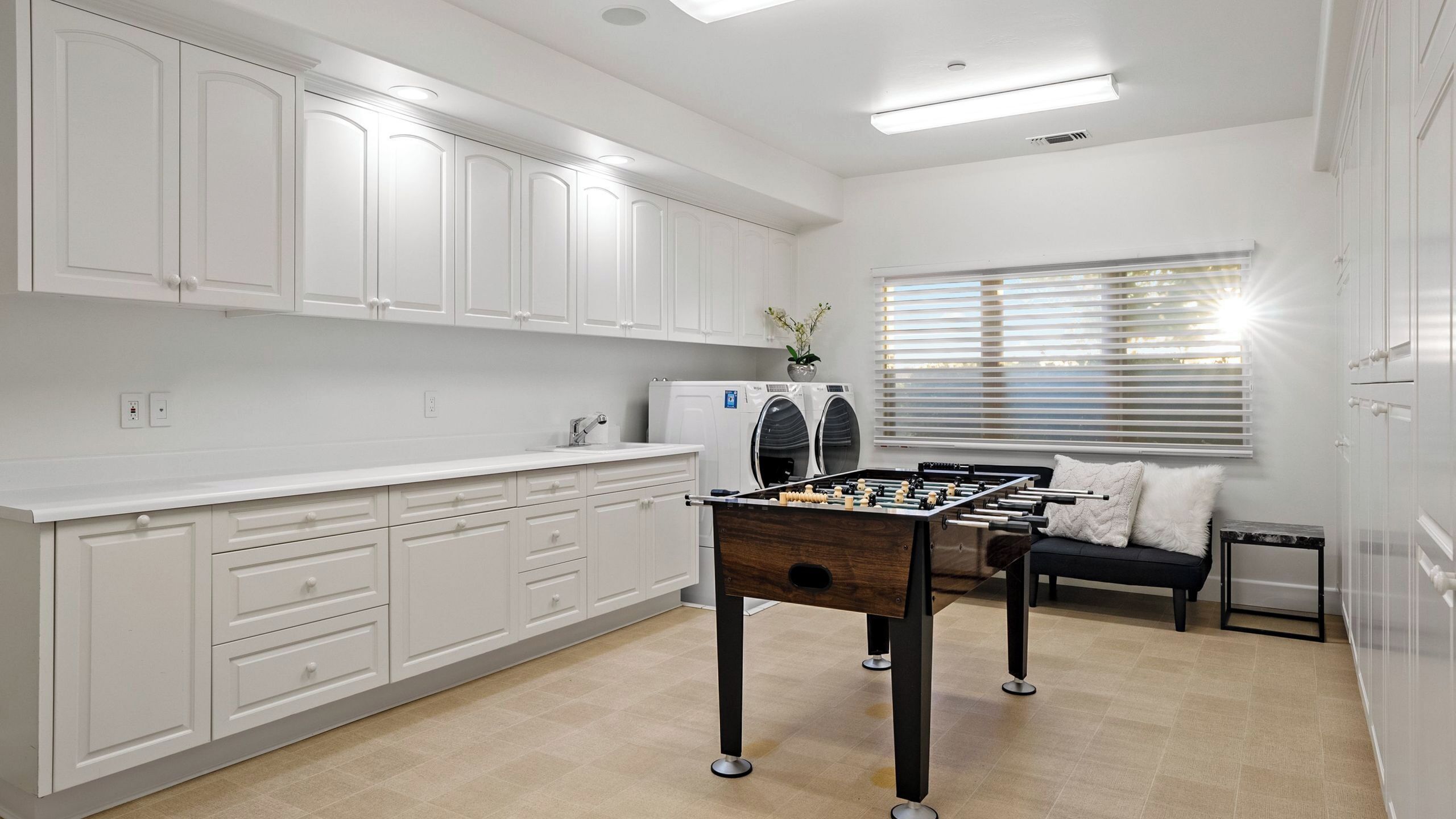 A modern kitchen with white cabinets, a built-in washing machine, and a foosball table.