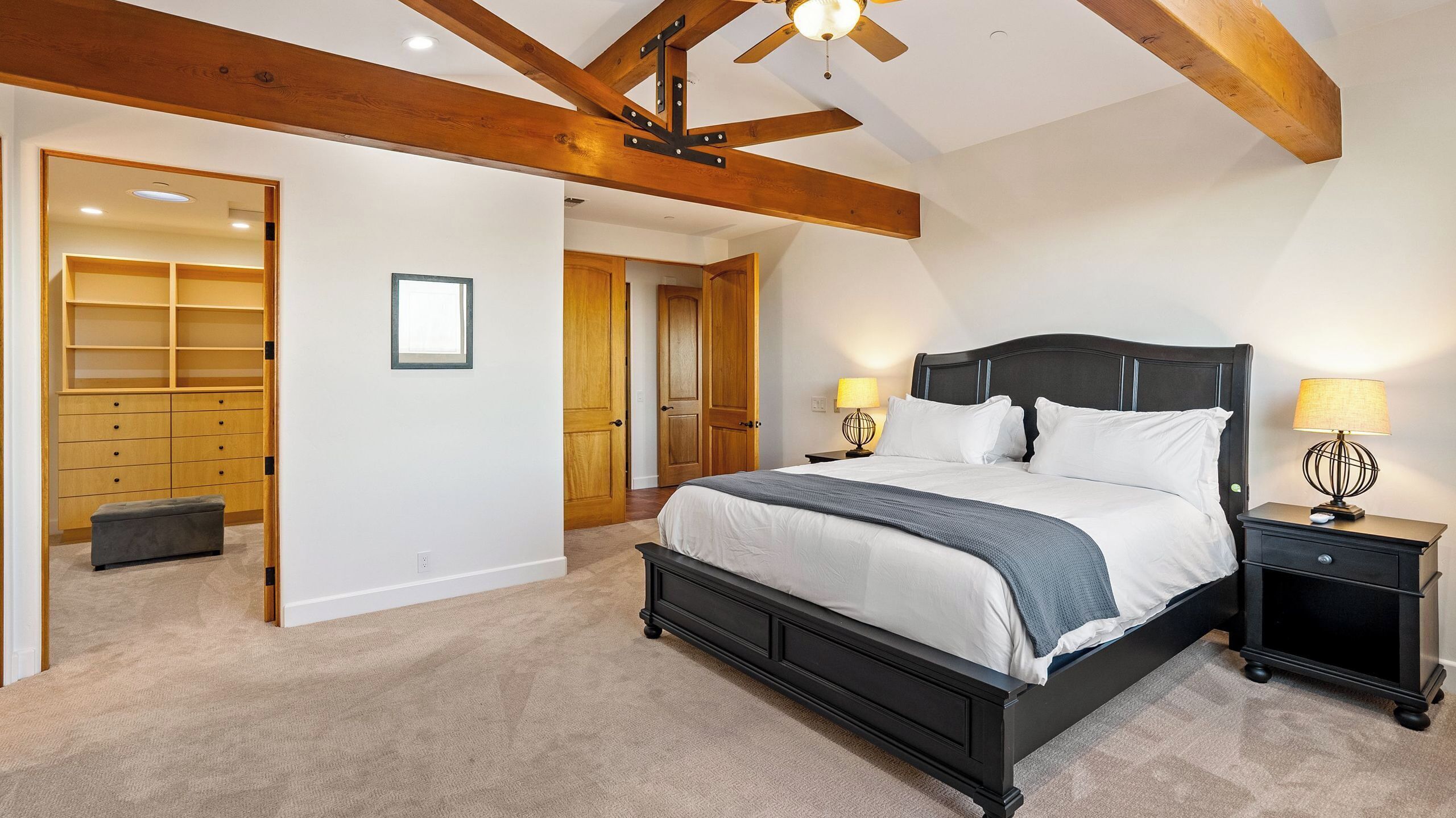 A bedroom with a large bed, two bedside tables with lamps, a ceiling fan, and a wardrobe with open doors.