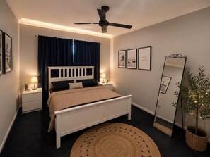 A bedroom with a bed, bedside tables, a ceiling fan, a mirror, and a potted plant.