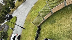 A white car parked on a curved road with a grassy area and a metal fence on the right.