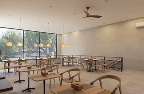 Un amplio comedor interior con varias mesas y sillas, ventanas grandes y lámparas colgantes.