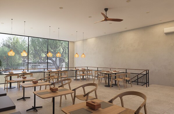 Un vaste espace de restauration intérieur, doté de nombreuses tables et chaises, de grandes fenêtres et de luminaires suspendus.