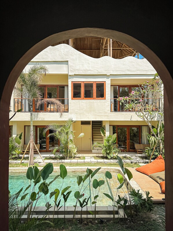 Un edificio de dos pisos con piscina, rodeado de plantas tropicales.
