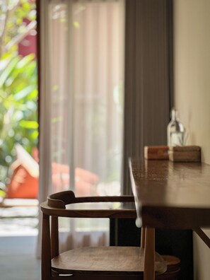 Una mesa de madera con una silla al frente, una botella sobre la mesa y vista a un paisaje verde al exterior.