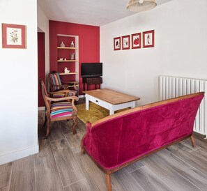 A living room with a wooden coffee table, a red velvet sofa, a striped armchair, and a television on a stand. - Lucette la mouette - Les Gîtes de la Côte d'Amour (BATZ SUR MER)