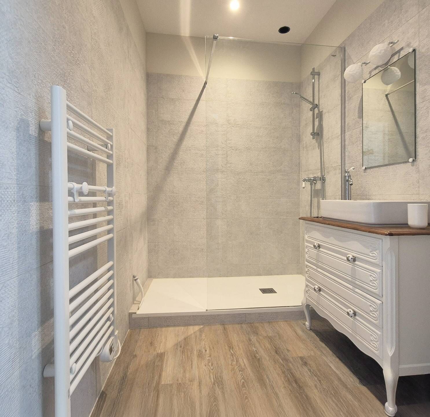 A modern bathroom with a walk-in shower, a white vanity with a mirror, and a wooden floor.