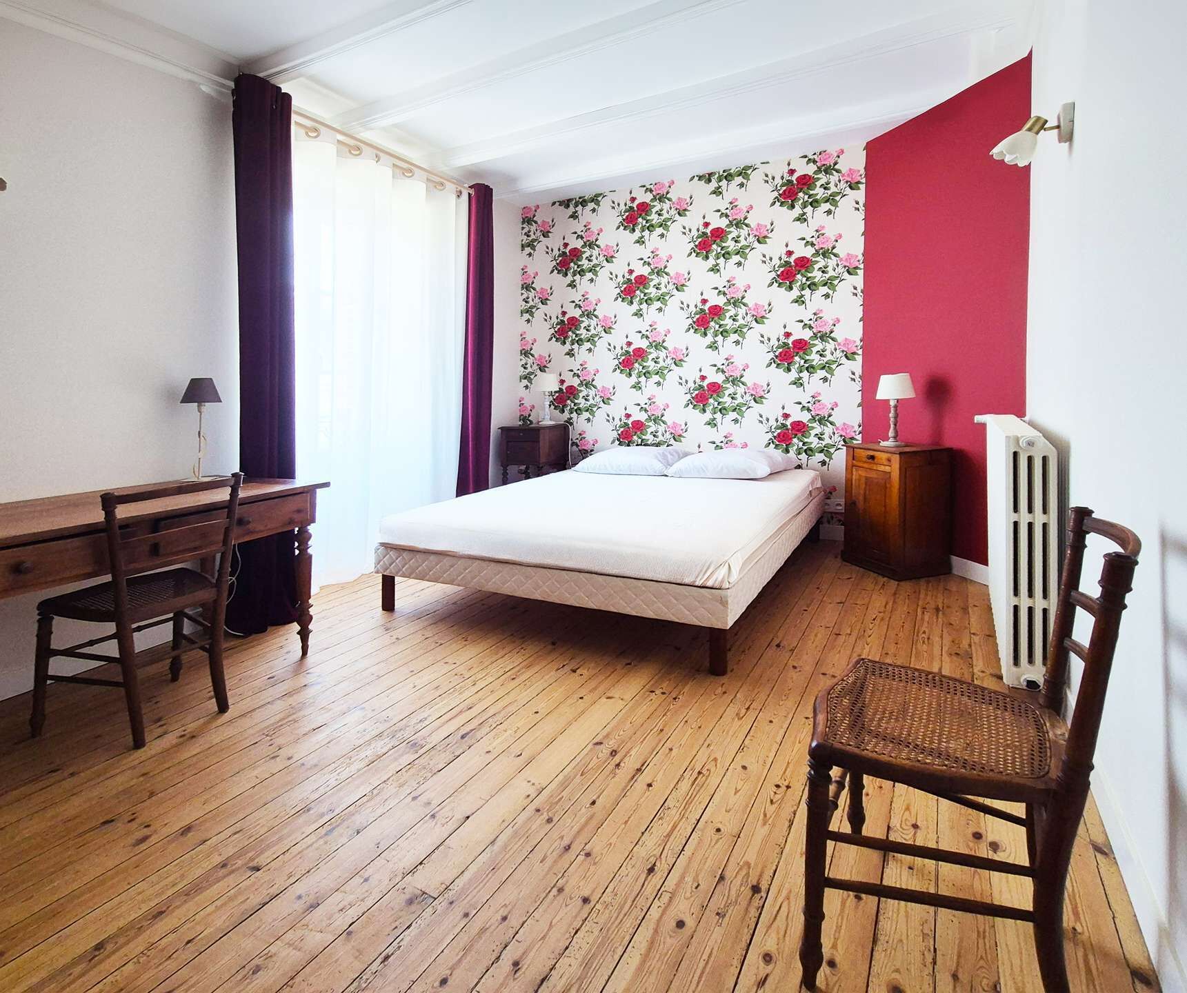 A bedroom with a bed, a desk, a chair, a radiator, and a window with curtains.