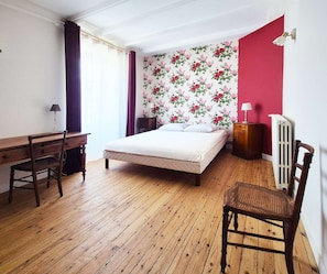 Ein Schlafzimmer mit Bett, Schreibtisch, Stuhl, Heizkörper und einem Fenster mit Vorhängen.