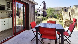 Um pátio com mesa e cadeiras, uma porta de correr e vista para o jardim.