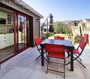 A patio with a table and chairs, a sliding glass door, and a garden view. - Lucette la mouette - Les Gîtes de la Côte d'Amour (BATZ SUR MER)