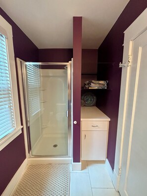 Ein Badezimmer mit Duschkabine aus Glas, einem weißen Schrank und einer violetten Wand.