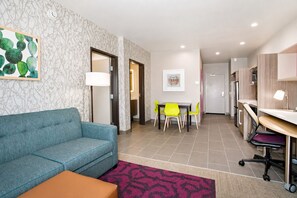 Ein modernes Hotelzimmer mit einer Sitzecke, einem Esstisch mit Stühlen, einer Küchenzeile und einem Badezimmer.