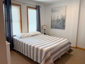 A bedroom with a bed, curtains, a lamp, and a painting. - The Dune Abides - Oceanfront, Private Yard with Pool, Hot Tub, Volleyball Court (Nags Head)