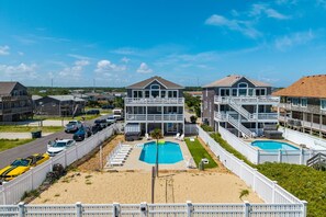 A beachfront property with two-story buildings, a swimming pool, and a sandy beach area. - The Dune Abides - Oceanfront, Private Yard with Pool, Hot Tub, Volleyball Court (Nags Head)