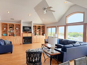 A spacious living room with a fireplace, built-in shelving, a television, and a large window offering a view.