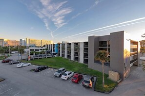 Ein modernes Gebäude mit Parkplatz, mehreren Autos und blauem Himmel mit Kondensstreifen.