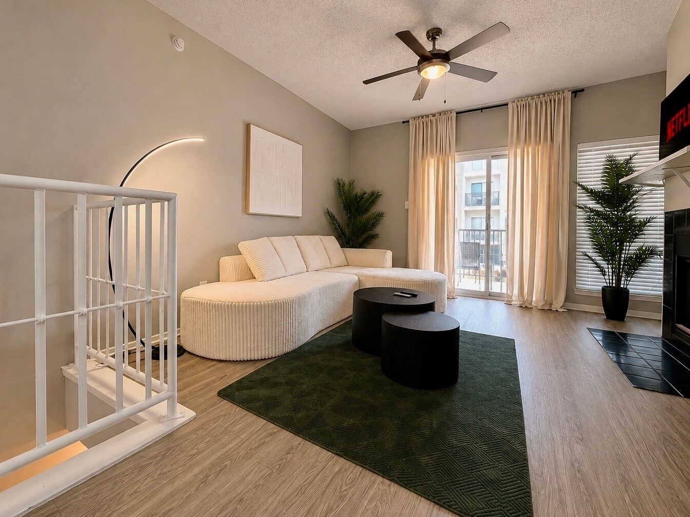 A modern living room with a sectional sofa, a ceiling fan, a TV, and a large window with curtains.