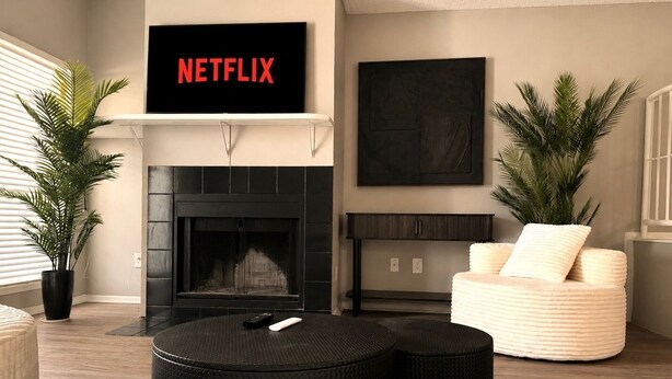 Ett vardagsrum med en öppen spis, en soffa, ett soffbord och en tv-skärm som visar ”NETFLIX”.