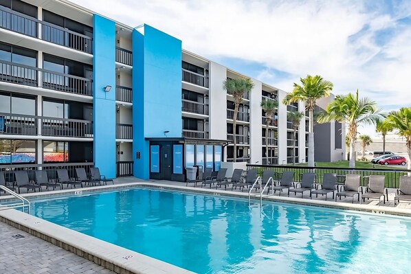 Ein modernes Hotel mit Schwimmbad, mehreren Balkonen und Palmen.
