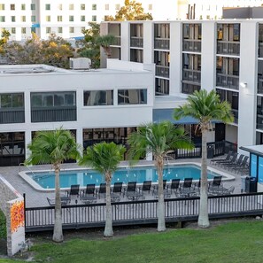 Ein modernes Hotel mit Poolanlage, Palmen und Blick auf die umliegenden Gebäude.