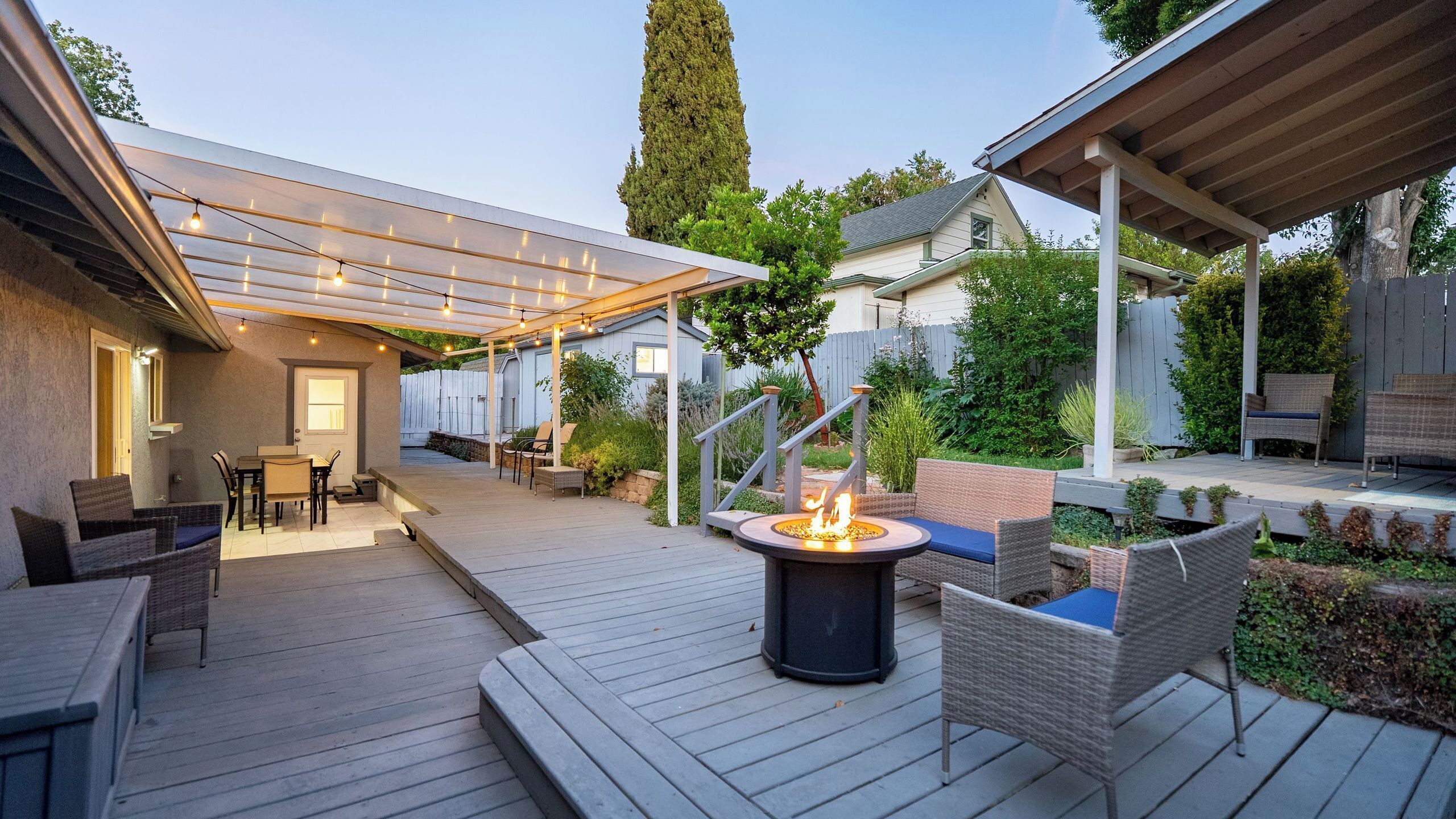 Un'area patio esterna con un braciere, posti a sedere e una zona riparata con luci decorative.
