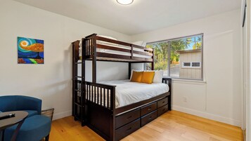 Una cama litera con ventana, un escritorio y una silla en una habitación con suelo de madera.