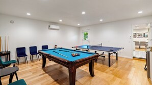 Una mesa de billar en una habitación con suelo de madera, una puerta con vistas y un aire acondicionado instalado en la pared.
