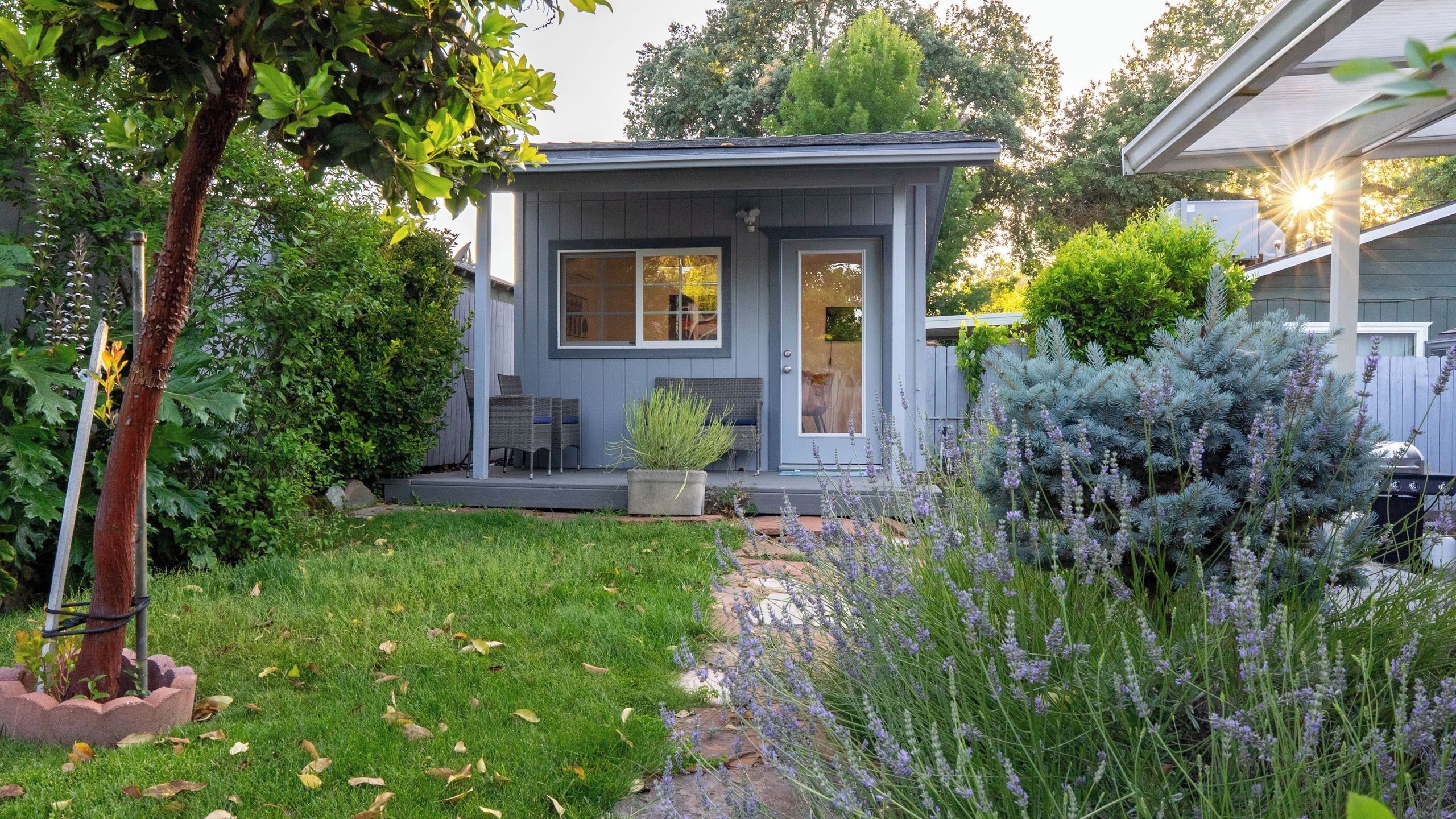A small house with a front porch, a potted plant, and a garden with lavender.