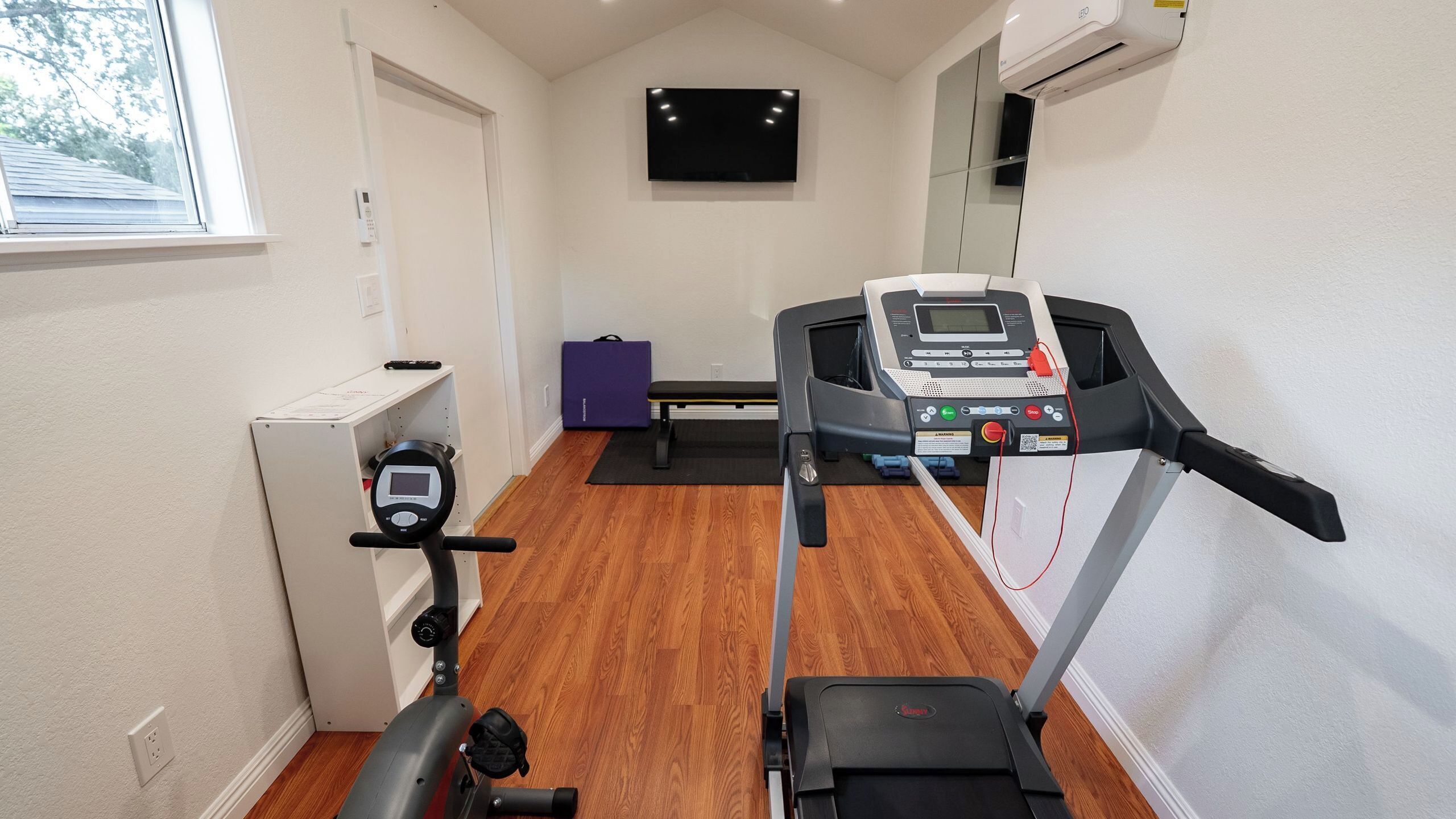 Ginásio em casa com esteira, bicicleta ergométrica e equipamentos de exercício.