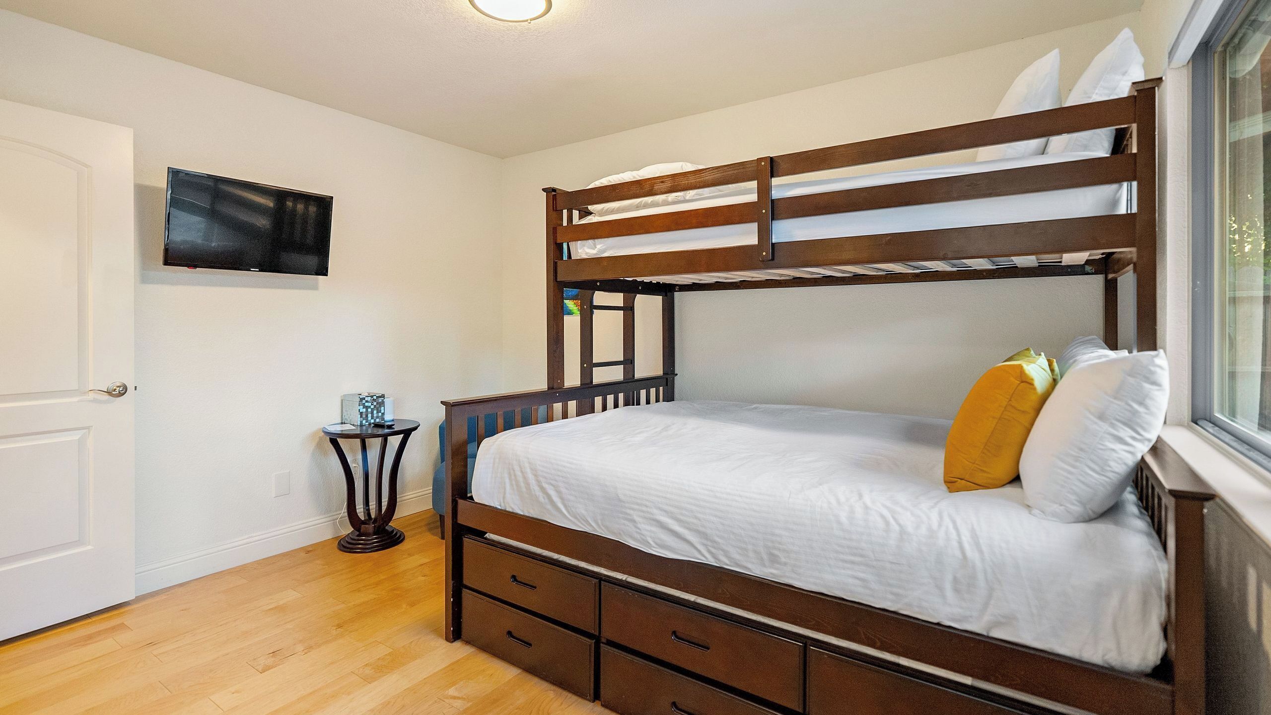 A bunk bed with a wooden frame, white bedding, and a small bedside table with a lamp.