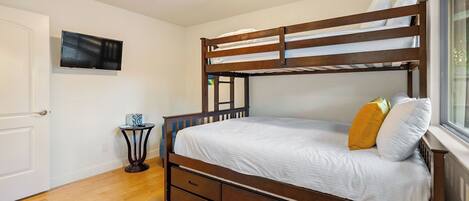 A bunk bed with a wooden frame, white bedding, and a small bedside table with a lamp.