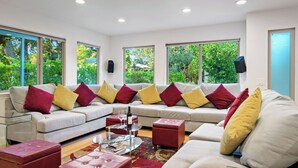 Una sala moderna con un sofá modular, cojines rojos y amarillos, una mesa de centro de vidrio y un otomano rojo.