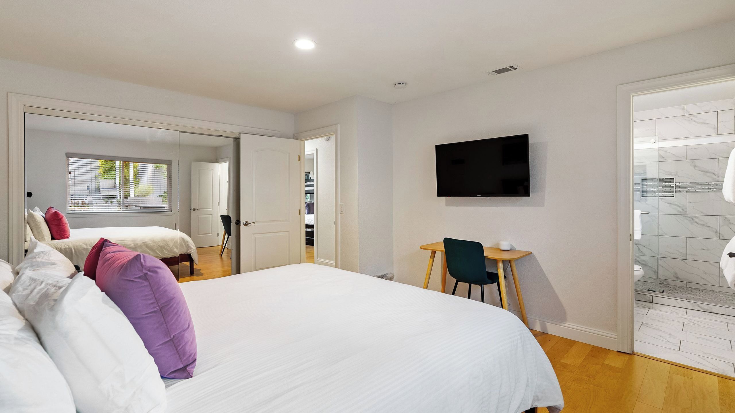 A hotel room with a large bed, a desk, a chair, a television, and a bathroom with a tiled wall.