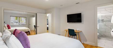 A hotel room with a large bed, a desk, a chair, a television, and a bathroom with a tiled wall.